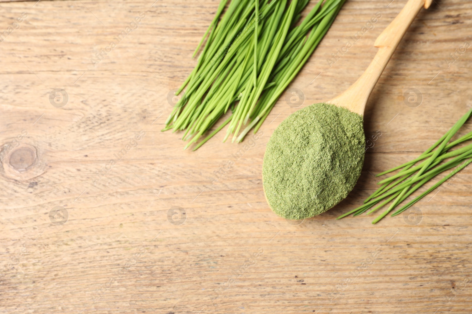 Photo of Wheat grass powder in spoon and fresh green sprouts on wooden table, flat lay. Space for text