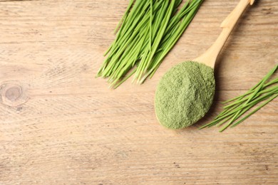 Photo of Wheat grass powder in spoon and fresh green sprouts on wooden table, flat lay. Space for text