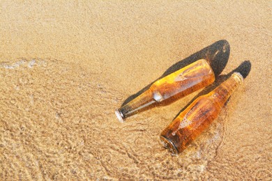 Photo of Bottles of cold beer in water on sandy beach, above view. Space for text