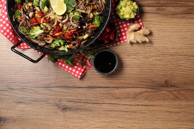 Photo of Stir-fry. Tasty noodles with meat in wok and ingredients on wooden table, flat lay. Space for text