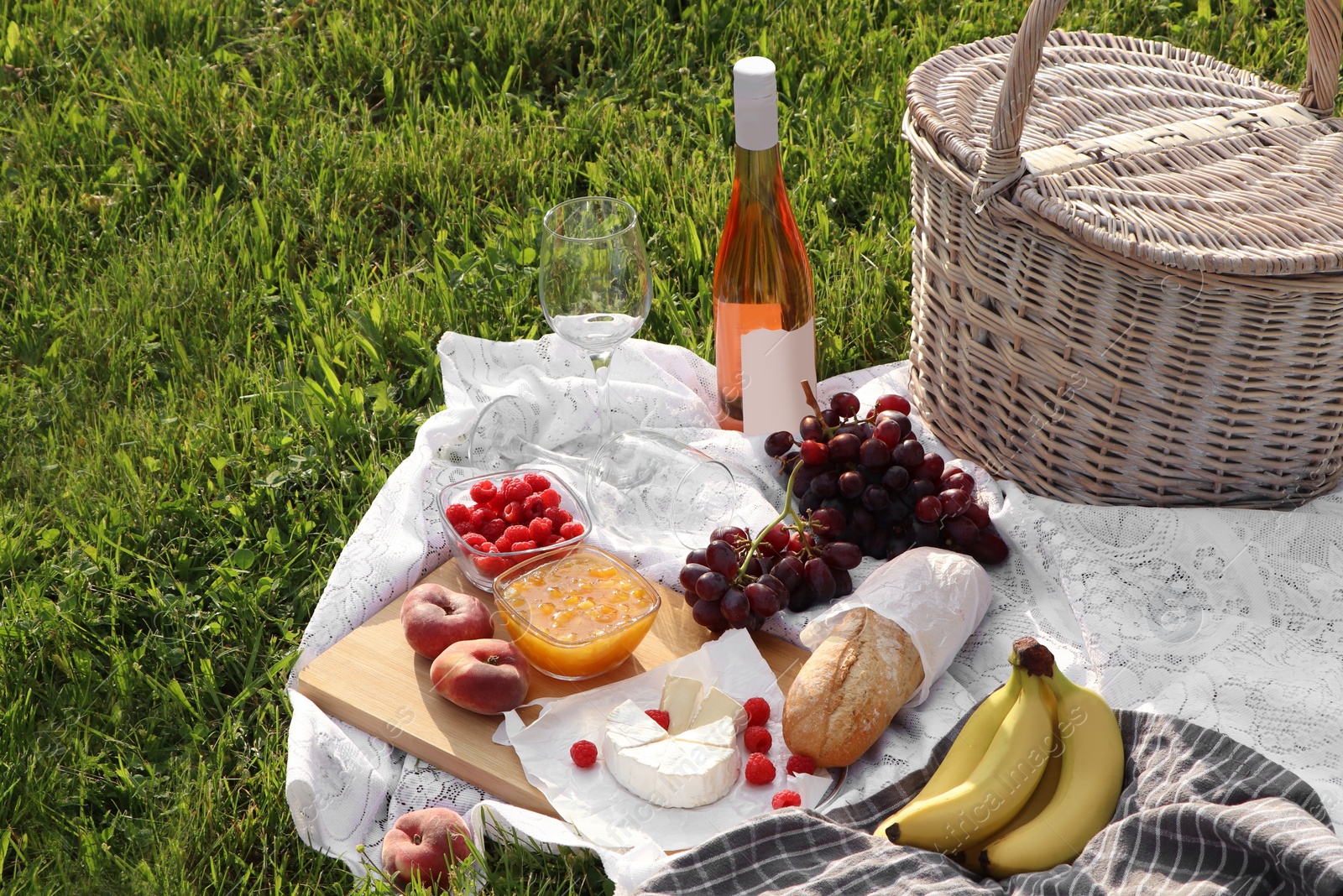 Photo of Picnic blanket with tasty food, basket and cider on green grass outdoors