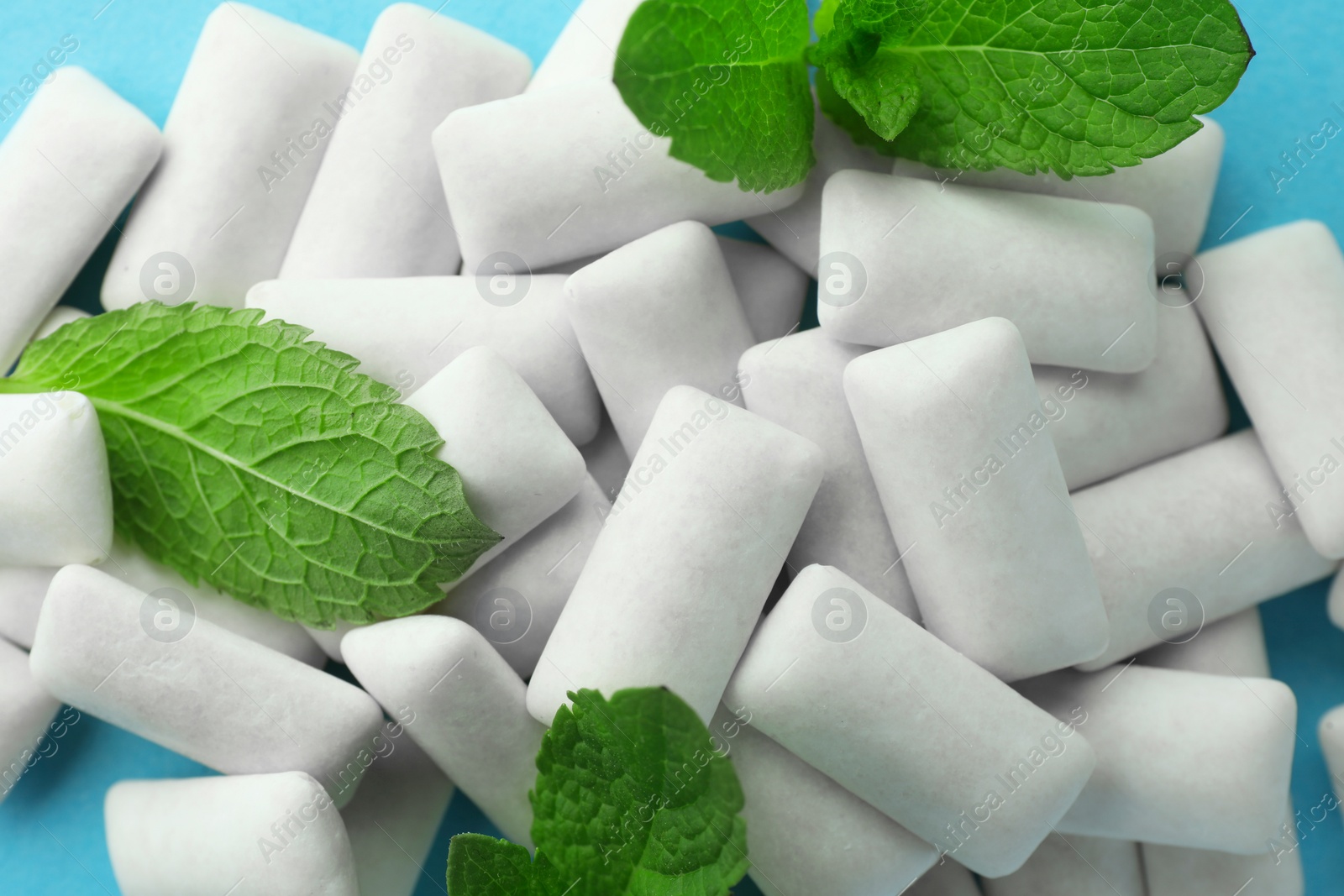 Photo of Pile of tasty white chewing gums and mint leaves on light blue background, top view