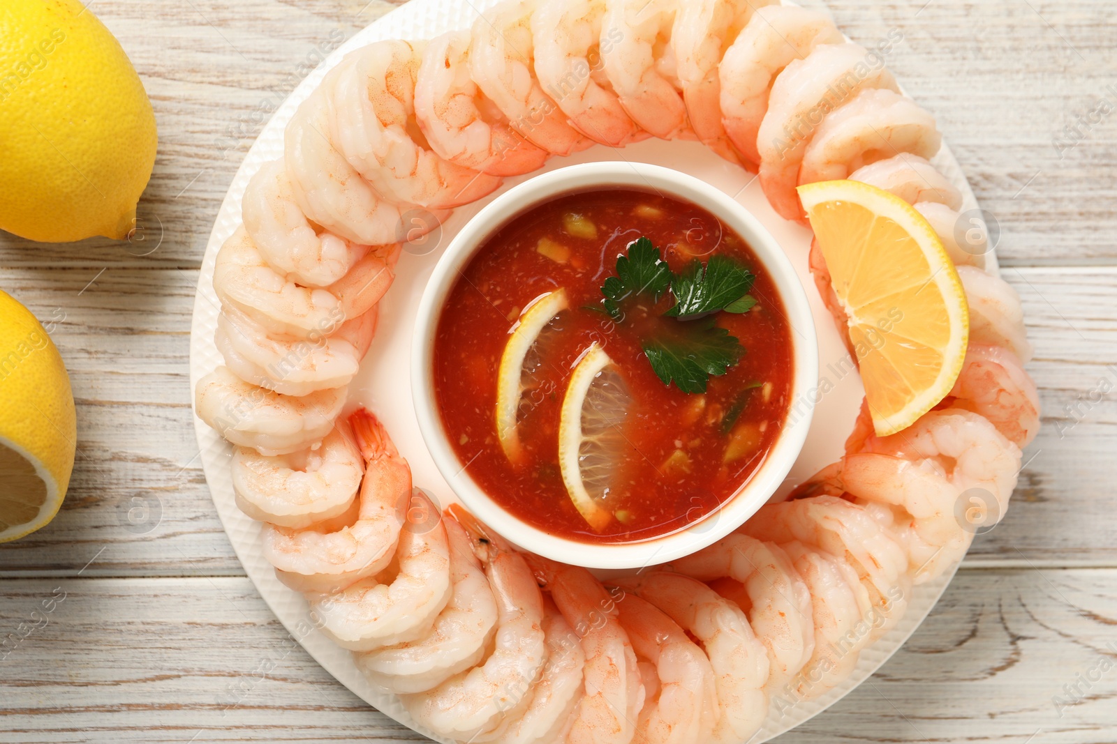 Photo of Tasty boiled shrimps with cocktail sauce and lemon on white wooden table, top view