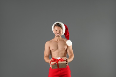 Shirtless sexy young Santa Claus with gift on color background