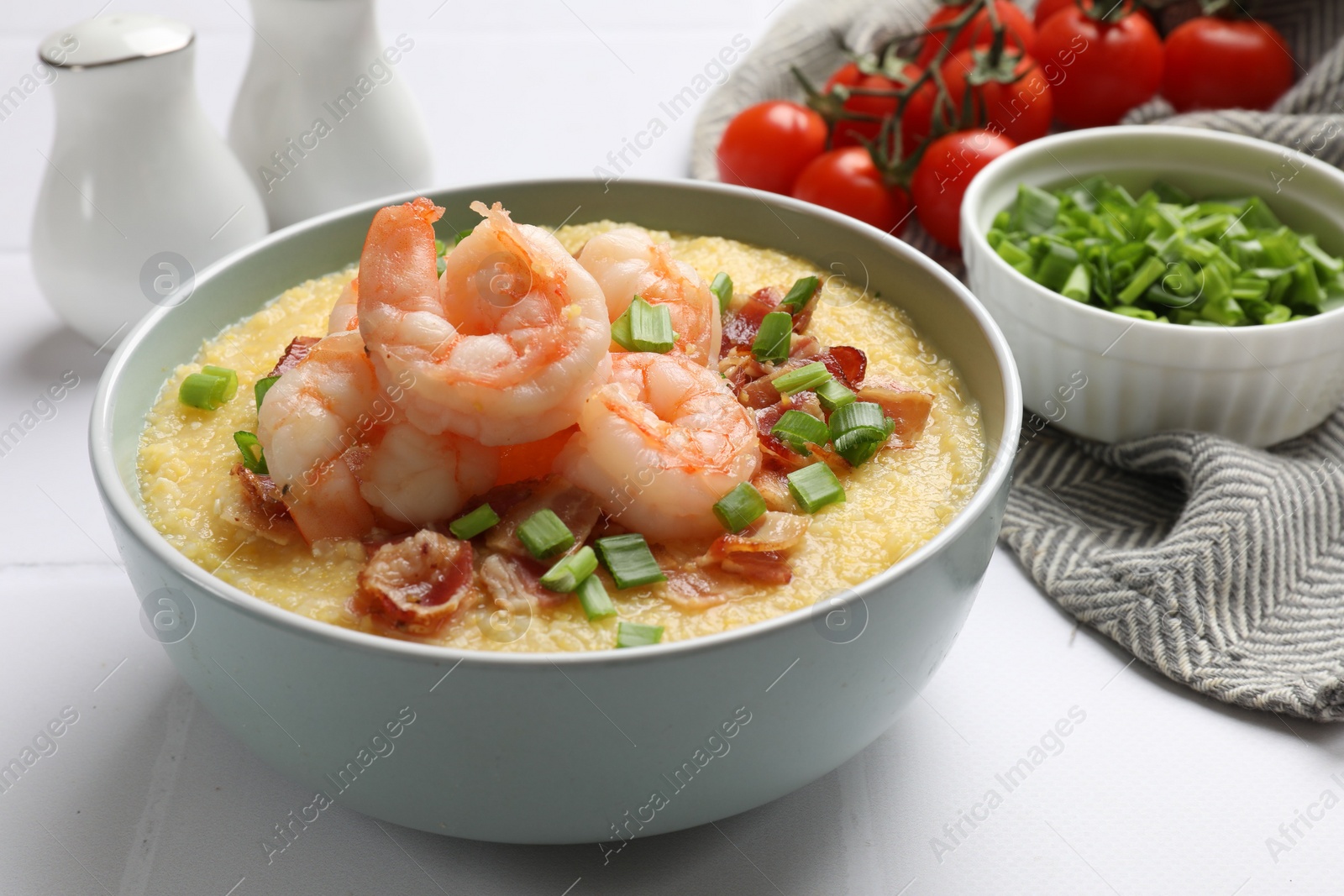 Photo of Fresh tasty shrimps, bacon, grits and green onion in bowl on white table, closeup