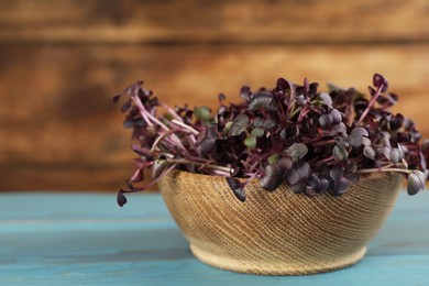 Photo of Fresh radish microgreens in bowl on turquoise wooden table, closeup
