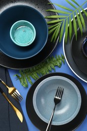 Flat lay composition with stylish ceramic plates and floral decor on blue background