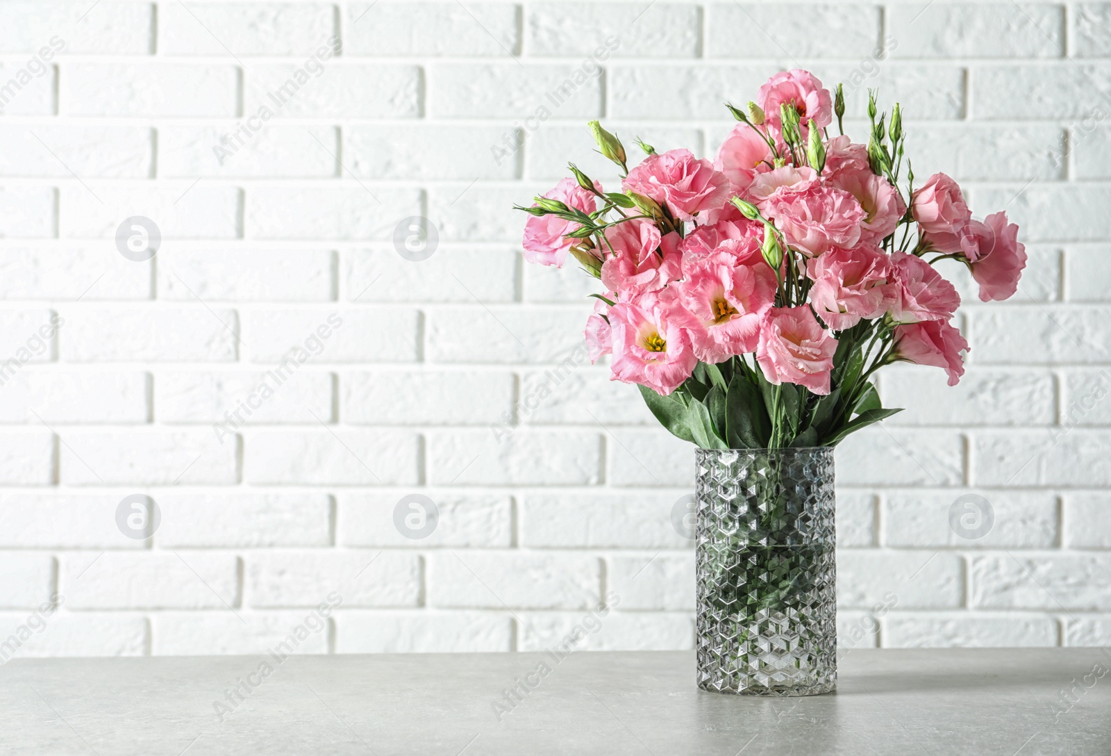 Photo of Vase with beautiful Eustoma flowers on table against brick wall