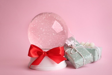 Beautiful empty snow globe and gift boxes on pink background