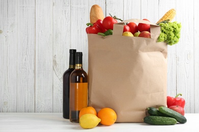 Photo of Shopping paper bag with different groceries on table against white wooden background. Space for text