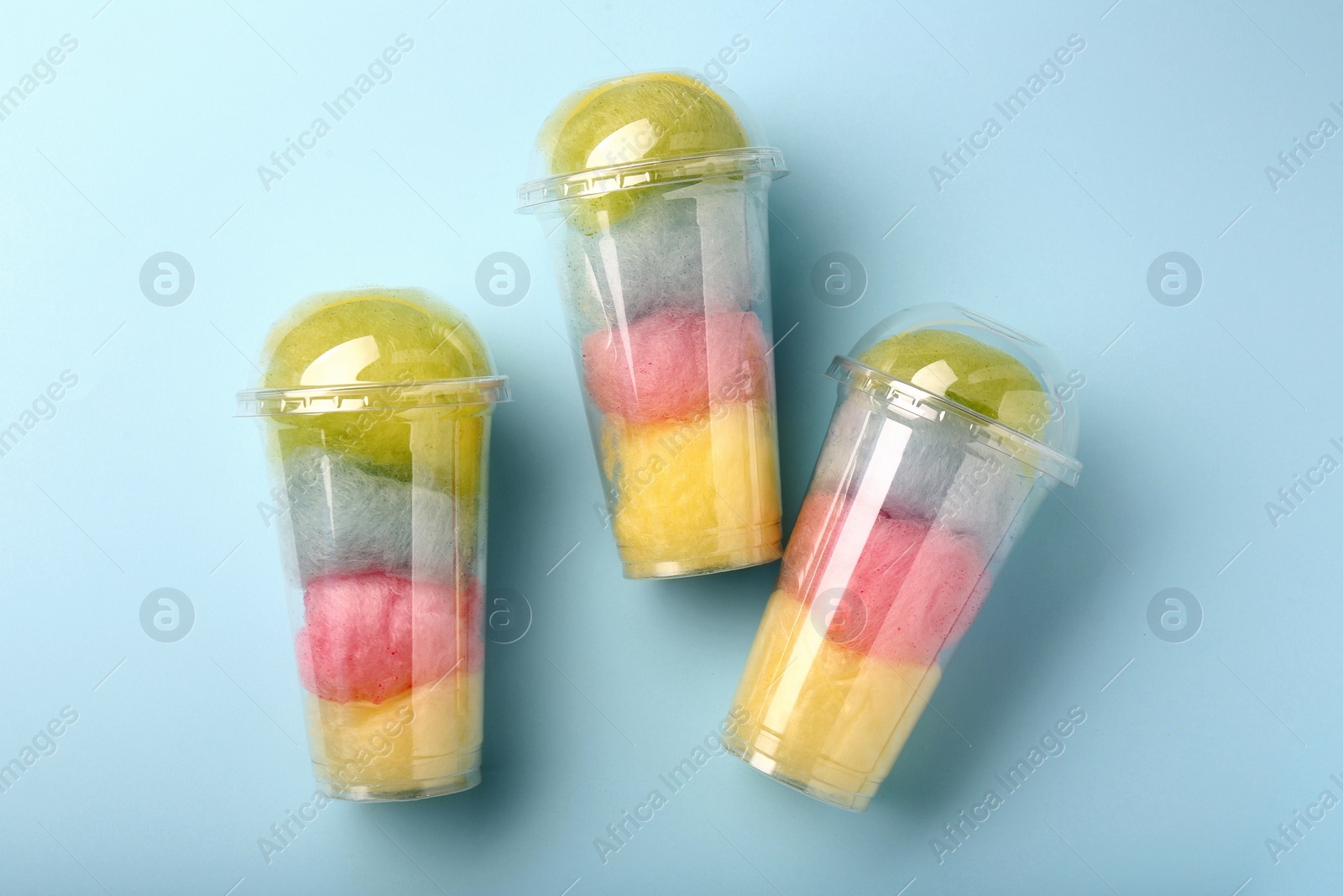 Photo of Colorful cotton candies in plastic cups on light blue background, flat lay