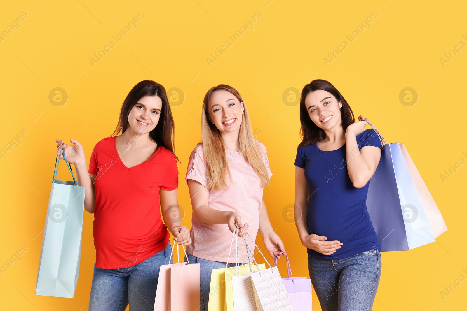 Photo of Happy pregnant women with shopping bags on orange background