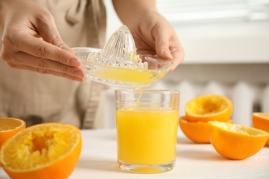 Photo of Woman pouring freshly made orange juice in glass at white table, closeup