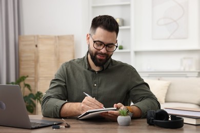 E-learning. Young man taking notes during online lesson at wooden table indoors