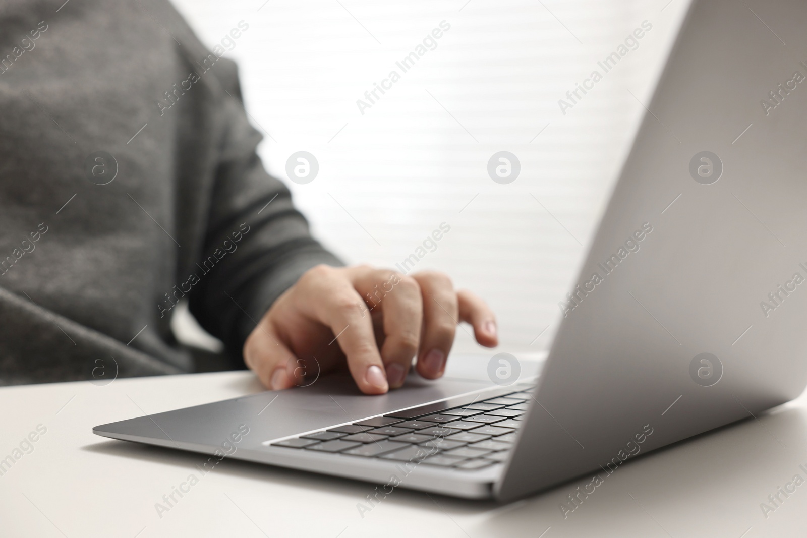 Photo of E-learning. Young man using laptop at white table, closeup