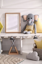 Empty photo frame and cute toy elephant near wall in baby room. Interior design