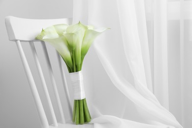 Beautiful calla lily flowers tied with ribbon on white chair indoors