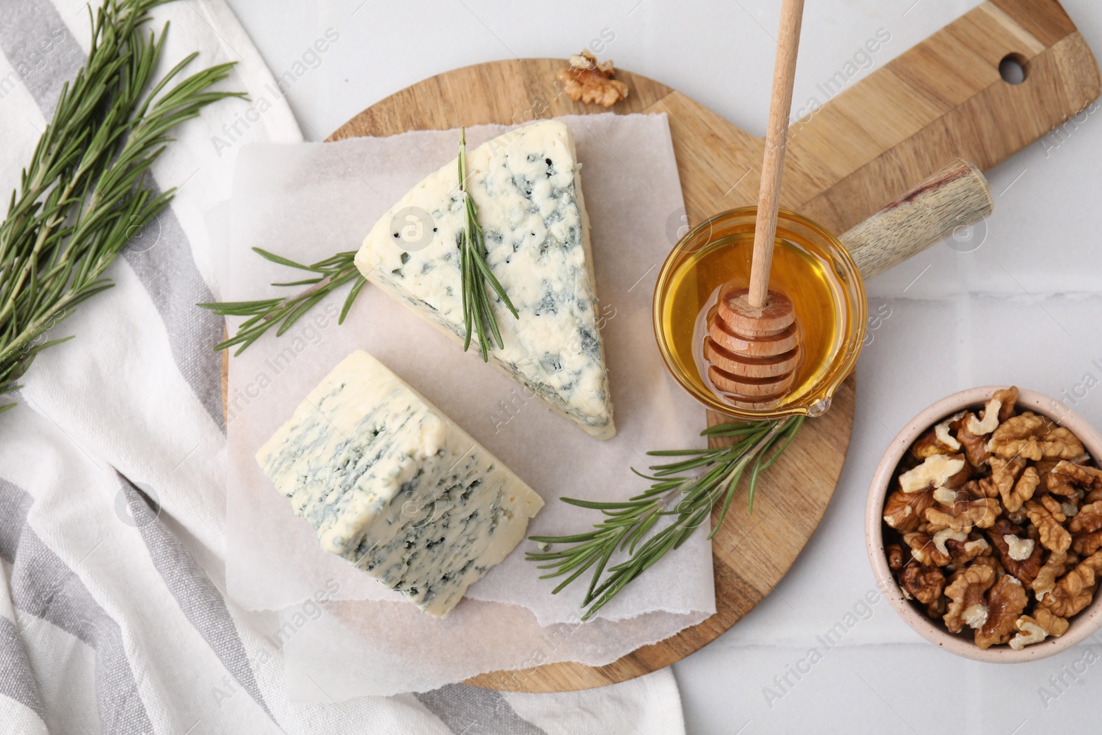 Photo of Tasty blue cheese with rosemary, honey and walnuts on white tiled table, flat lay