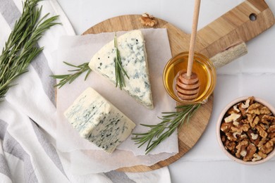 Tasty blue cheese with rosemary, honey and walnuts on white tiled table, flat lay