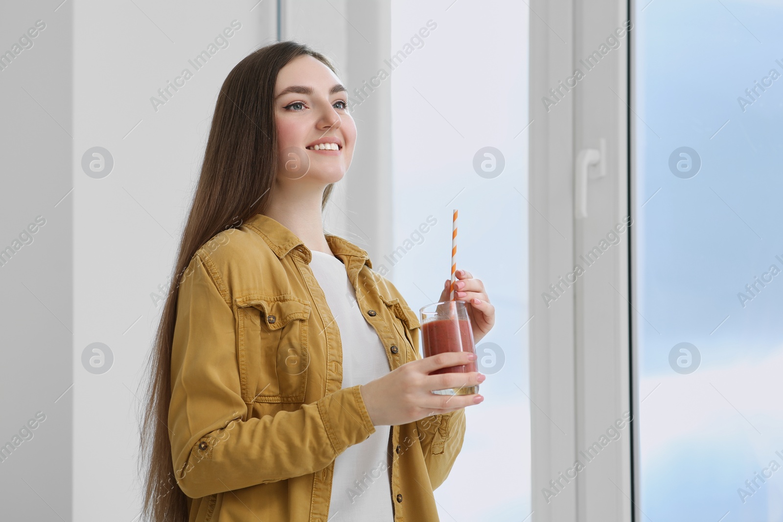 Photo of Beautiful young woman with delicious smoothie near window indoors. Space for text