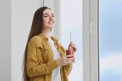 Photo of Beautiful young woman with delicious smoothie near window indoors. Space for text