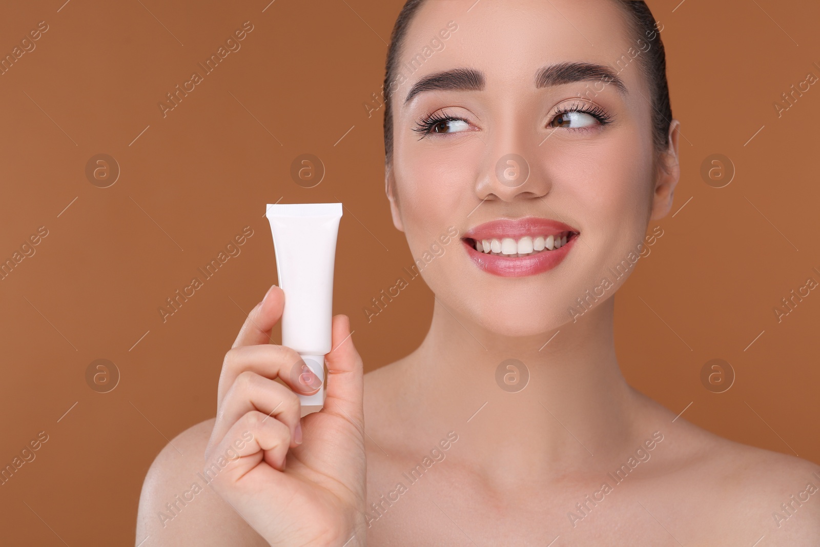 Photo of Woman holding tube of foundation on brown background