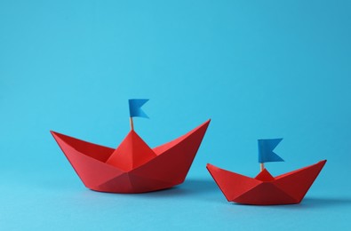 Photo of Two handmade red paper boats with flags on light blue background. Origami art