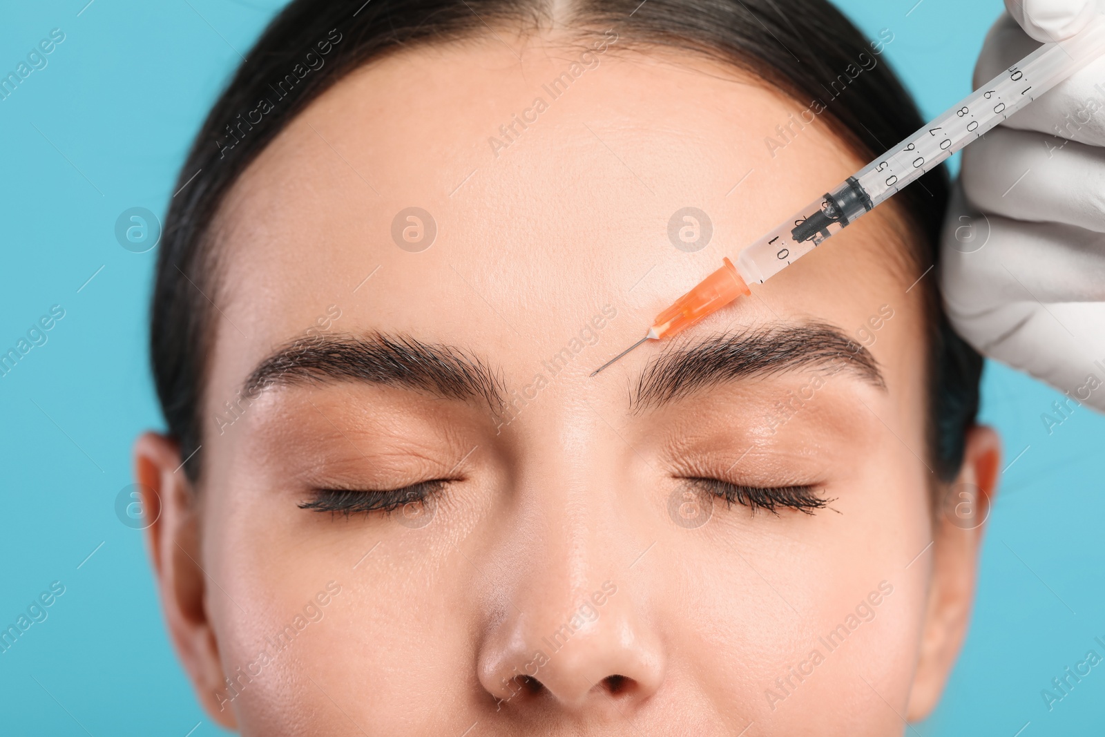 Photo of Doctor giving facial injection to young woman on light blue background, closeup. Cosmetic surgery