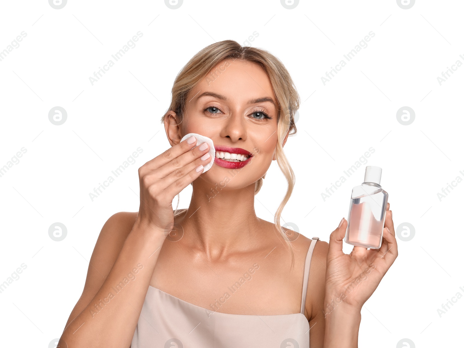 Photo of Smiling woman removing makeup with cotton pad and holding bottle on white background