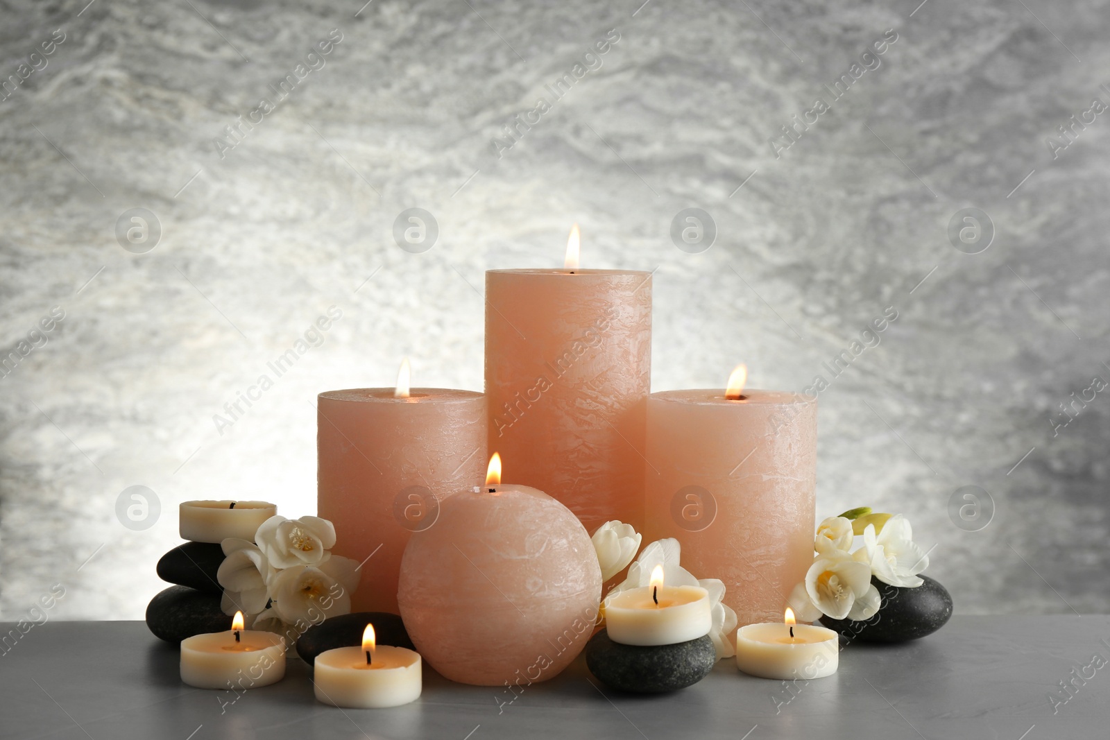 Photo of Beautiful composition with candles, flowers and stones on table against light background