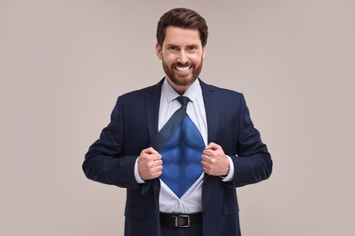 Happy businessman wearing superhero costume under suit on light grey background