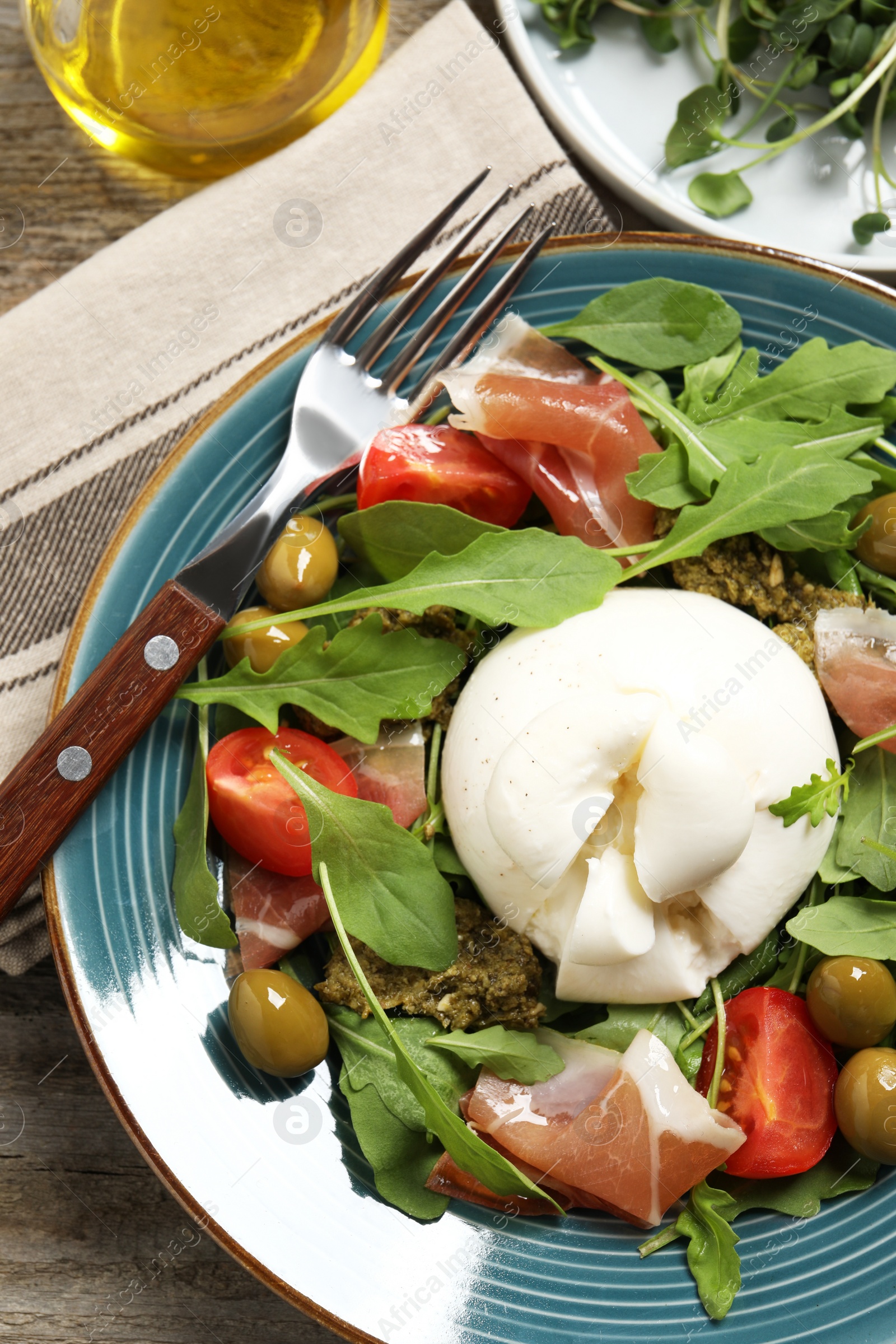 Photo of Delicious burrata salad served on wooden table, flat lay