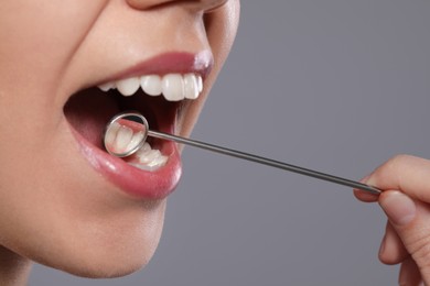 Photo of Dentist examining woman's teeth with mirror on grey background, closeup