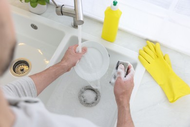 Photo of Man washing plate in kitchen sink, above view