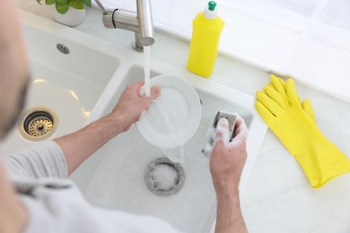 Man washing plate in kitchen sink, above view