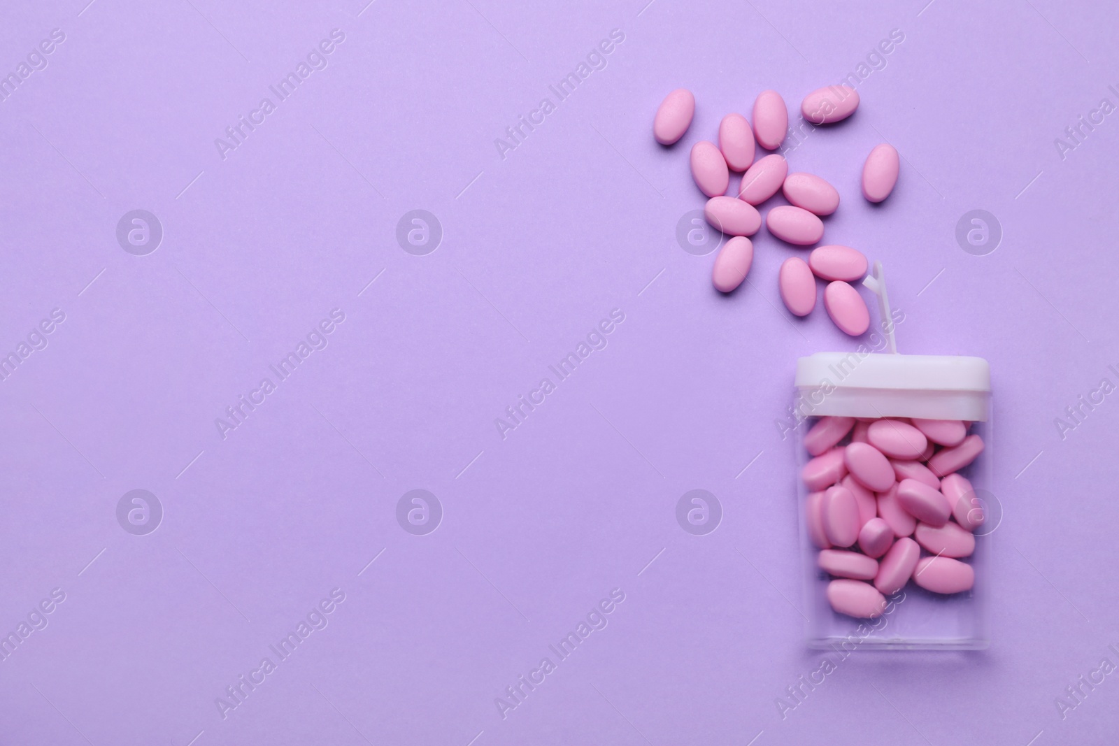 Photo of Tasty pink dragee candies and container on lilac background, flat lay. Space for text