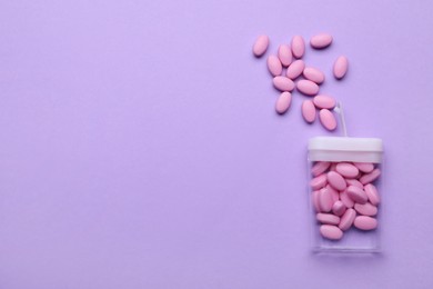 Photo of Tasty pink dragee candies and container on lilac background, flat lay. Space for text