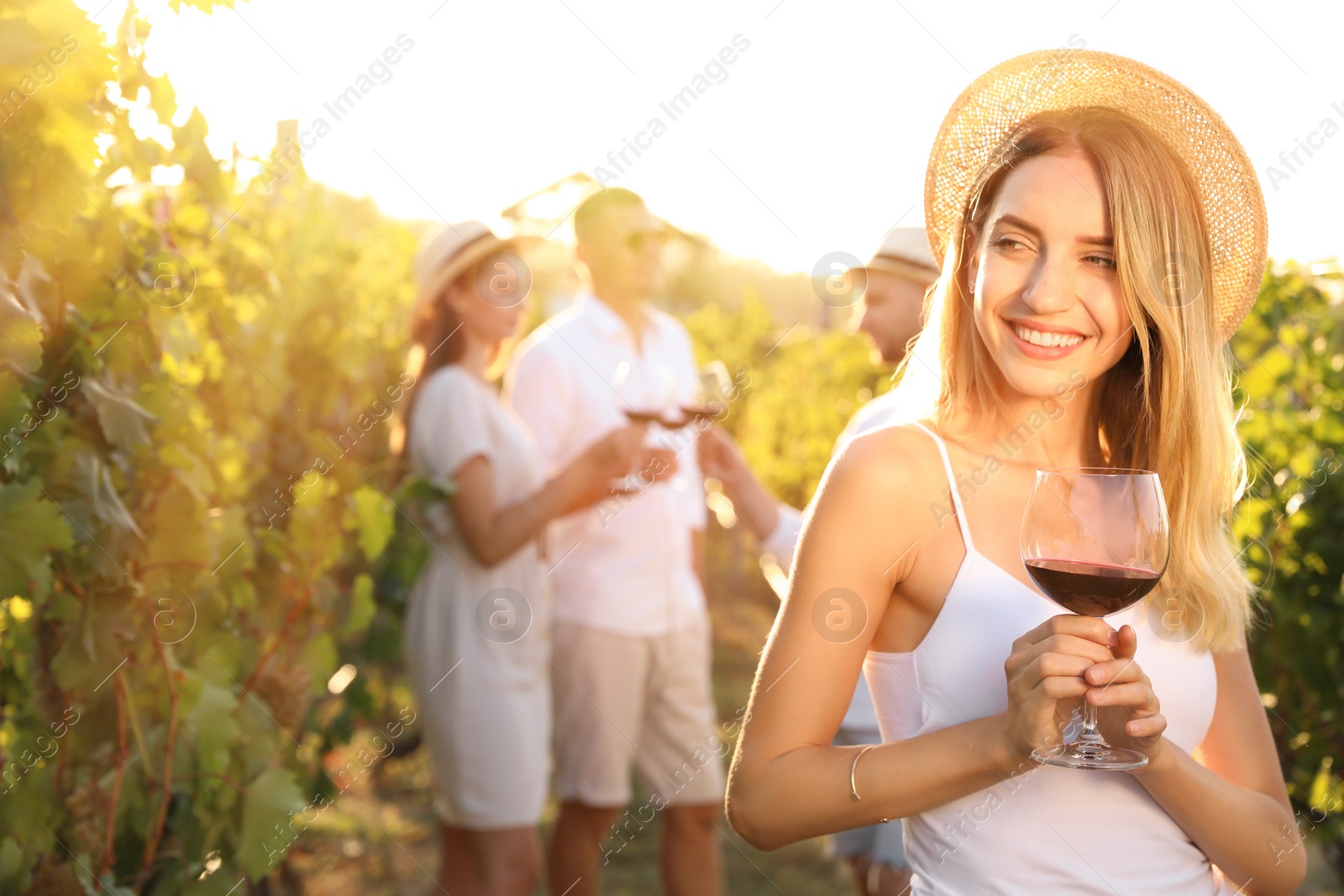 Photo of Beautiful young woman with glass of wine and her friends at vineyard on sunny day