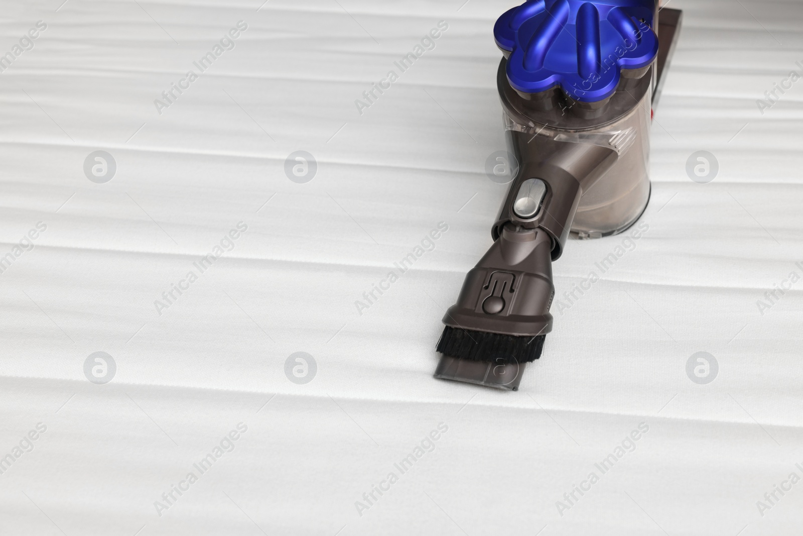 Photo of Modern vacuum cleaner on white mattress. Space for text