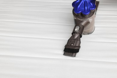 Photo of Modern vacuum cleaner on white mattress. Space for text