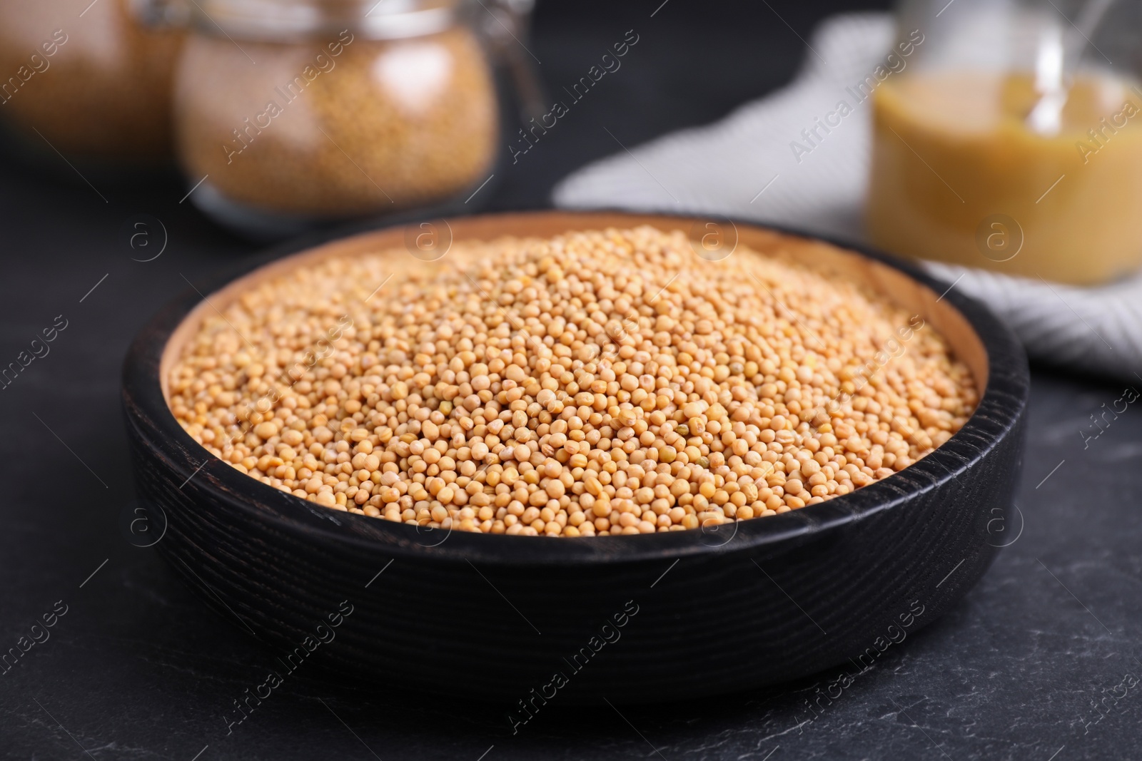 Photo of Mustard seeds in black bowl on grey table, closeup