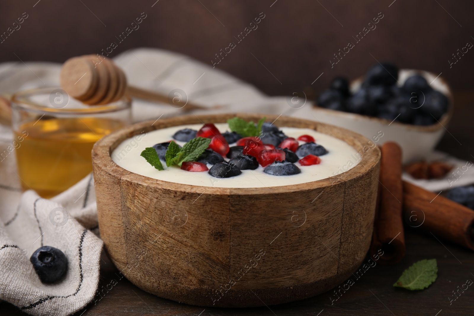 Photo of Bowl of delicious semolina pudding with blueberries, pomegranate and mint on table, closeup