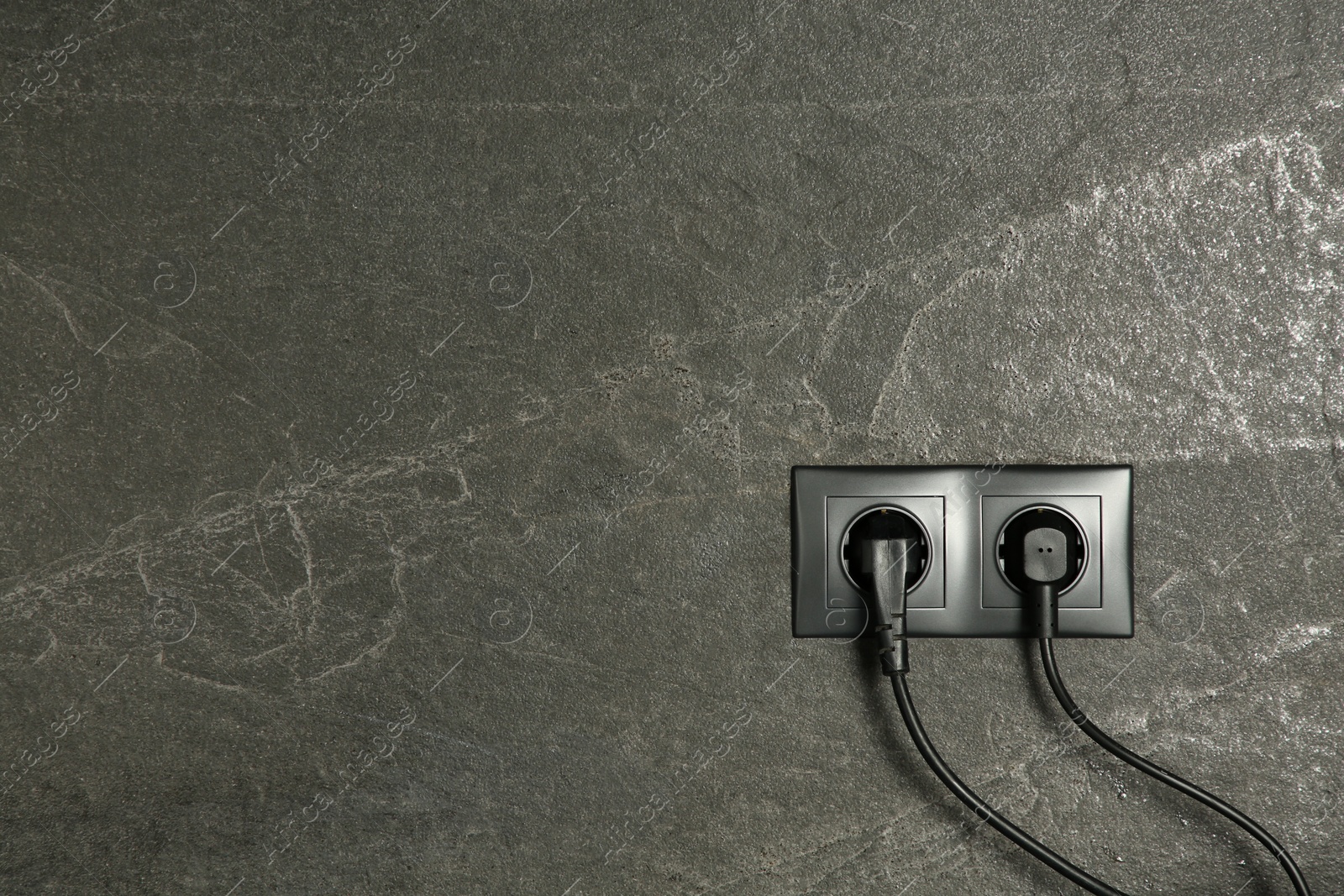 Photo of Power sockets with inserted plugs on dark grey wall, space for text. Electrical supply