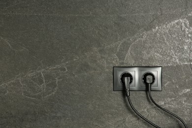 Photo of Power sockets with inserted plugs on dark grey wall, space for text. Electrical supply