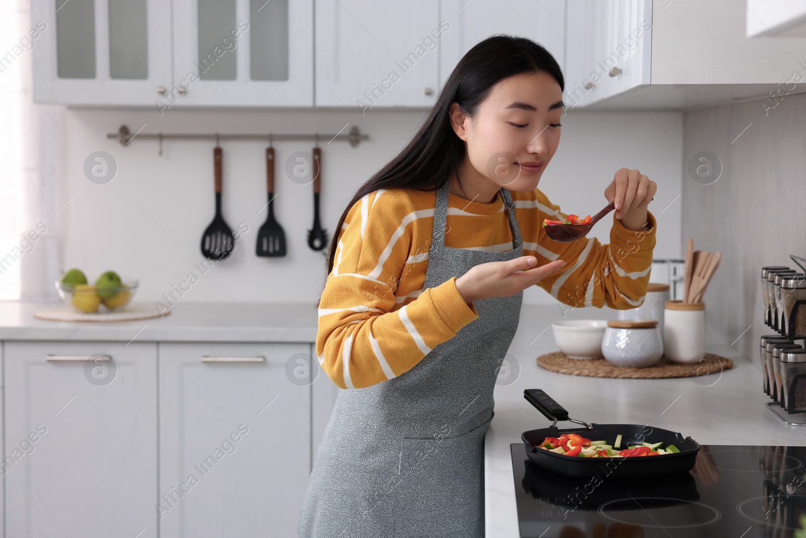 Photo of Beautiful woman cooking and tasting vegetable dish in kitchen. Space for text