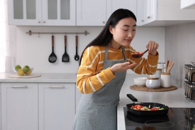 Beautiful woman cooking and tasting vegetable dish in kitchen. Space for text