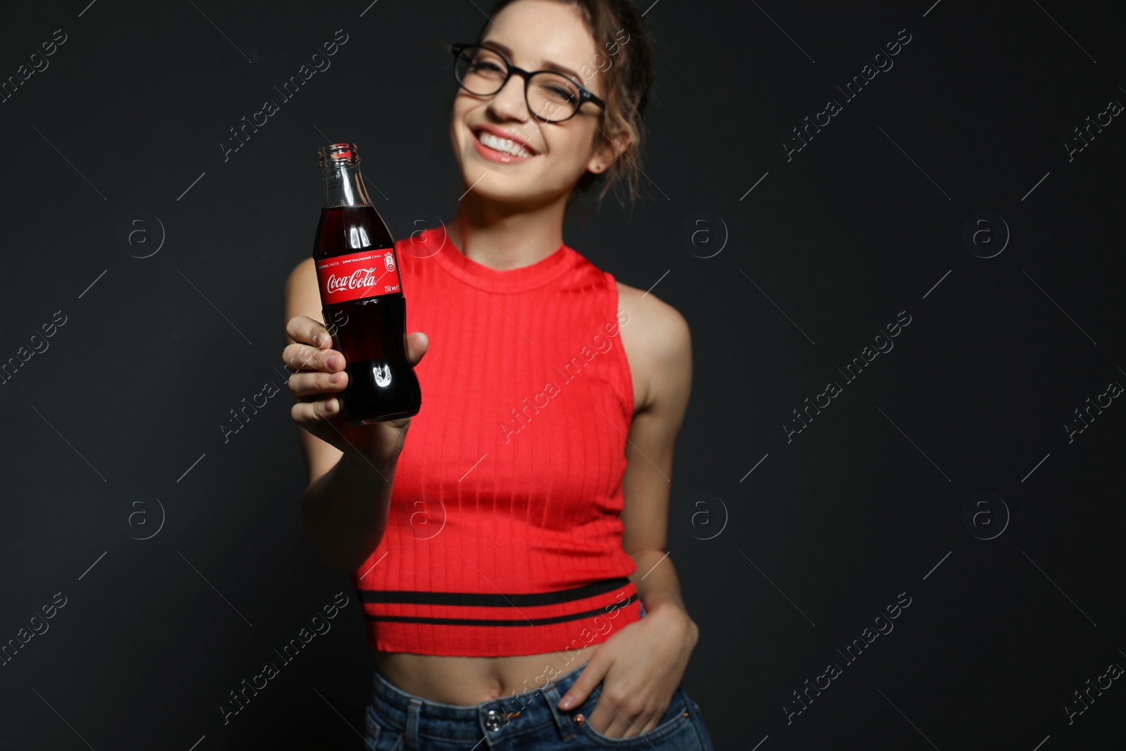 Photo of MYKOLAIV, UKRAINE - NOVEMBER 28, 2018: Young woman with bottle of Coca-Cola on dark background