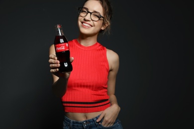 Photo of MYKOLAIV, UKRAINE - NOVEMBER 28, 2018: Young woman with bottle of Coca-Cola on dark background