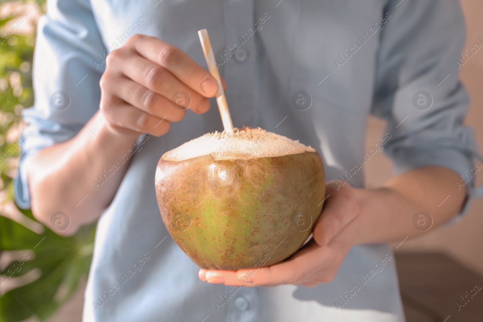 Photo of Young woman with fresh coconut cocktail on blurred background, closeup