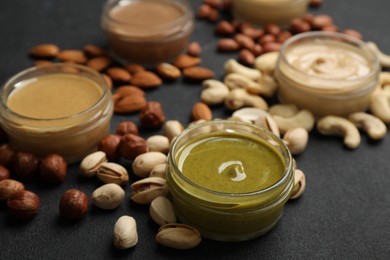 Jars with butters made of different nuts and ingredients on black table, closeup